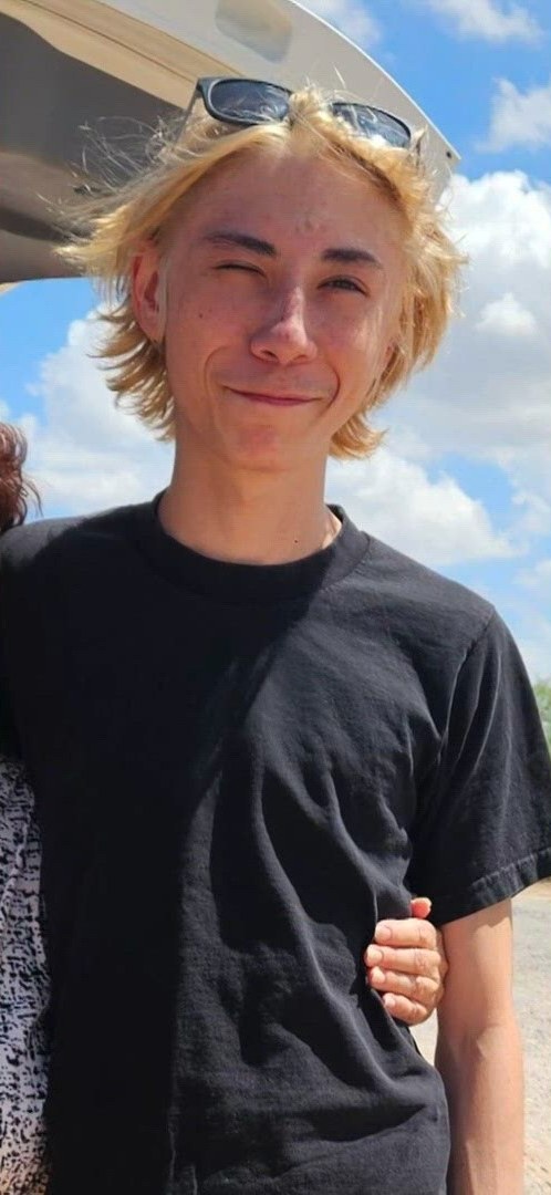Logan Almodova in a black t-shirt, smiling and winking outdoors on a sunny day
